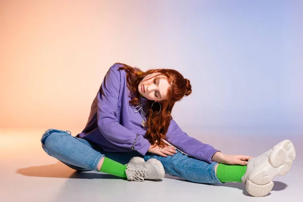 Hermosa aburrido adolescente chica con el pelo rojo sentado en púrpura y beige - foto de stock