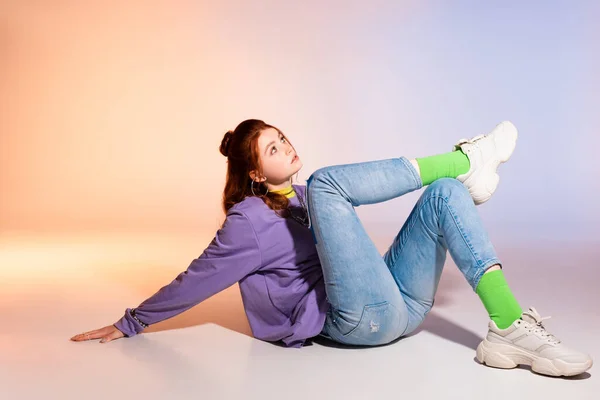 Beautiful bored female teenager sitting on purple and beige — Stock Photo