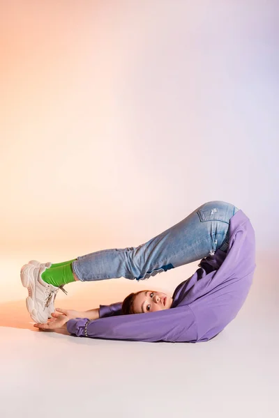 Sad redhead female teenager lying with legs up, on purple and beige — Stock Photo