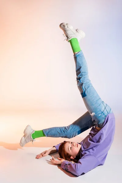 Hermosa pelirroja adolescente con las piernas arriba, en púrpura y beige - foto de stock