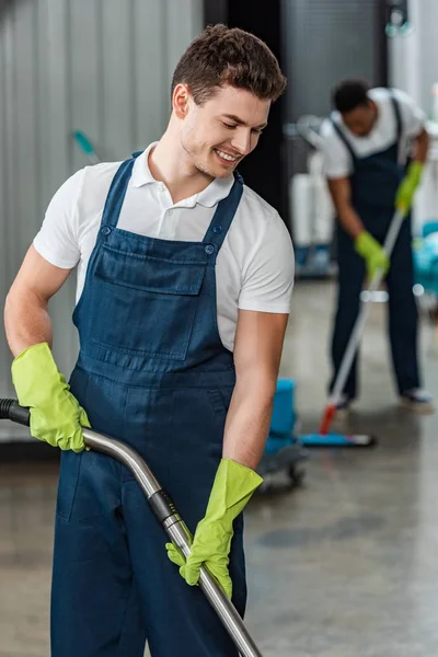 Messa a fuoco selettiva del detergente sorridente vicino al pavimento di lavaggio del collega africano americano con mop — Foto stock