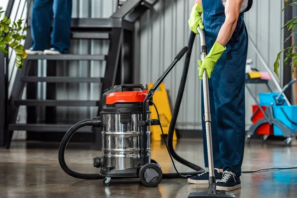 Cropped view of cleaner in uniform cleaning floor with vacuum cleaner — Stock Photo