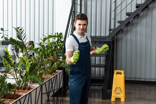 Handsome young cleaner in overalls and rubber gloves looking at camera — Stock Photo