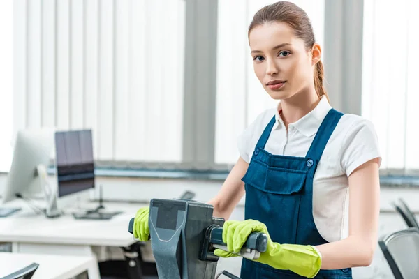 Attraktive Reinigungskraft in Overalls, die im Stehen mit Reinigungsmaschine in die Kamera schaut — Stockfoto