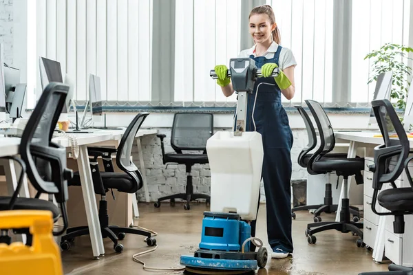 Limpiador sonriente lavado piso en la oficina con la máquina de limpieza - foto de stock