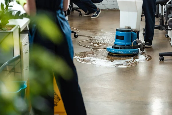 Cropped view of cleaner washing floor with cleaning machine near colleagues — Stock Photo