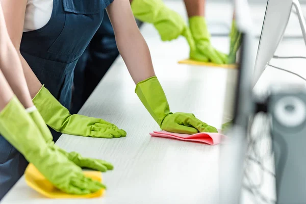 Cropped view of cleaners in rubber gloves cleaning office desk — Stock Photo