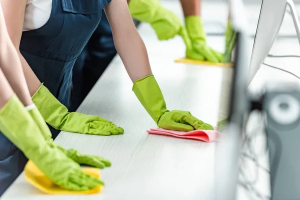 Vista recortada de limpiadores en guantes de goma escritorio de oficina de limpieza - foto de stock