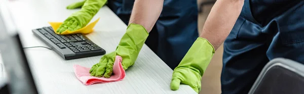 Vista parcial de limpiadores en guantes de goma escritorio de oficina de limpieza y teclado del ordenador - foto de stock