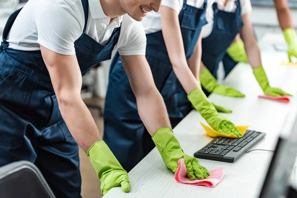 Ausgeschnittener Blick auf junge Reinigungskräfte, die Schreibtische mit Lumpen im Büro wischen — Stockfoto