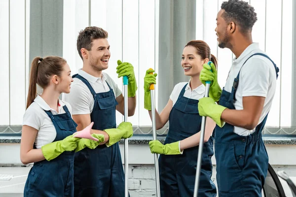 Sorrindo equipe multicultural de limpadores falando enquanto estava no escritório — Fotografia de Stock