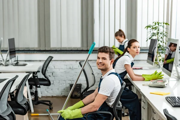 Equipo de jóvenes limpiadores sentados en la oficina moderna y mirando a la cámara - foto de stock