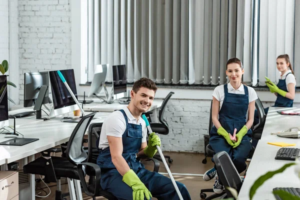 Équipe souriante de nettoyeurs assis dans un bureau moderne et regardant la caméra — Photo de stock