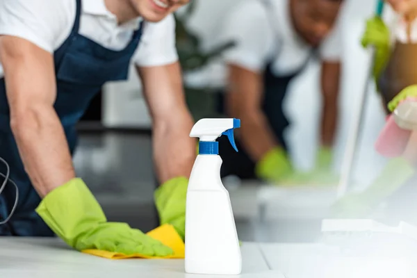 Ausgeschnittener Blick auf Putzfrau wischt Schreibtisch in der Nähe Sprühflasche mit Waschmittel — Stockfoto