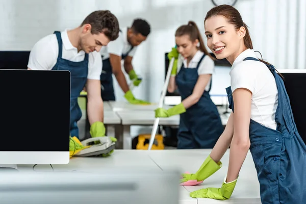 Selective focus of young cleaners wiping phone and desk near multicultural colleagues — Stock Photo