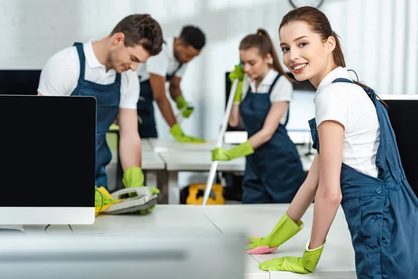 Selective focus of young cleaners wiping phone and desk near multicultural colleagues — Stock Photo