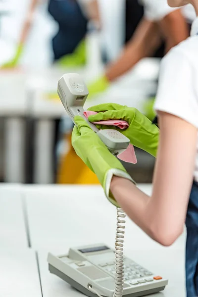 Частковий вигляд прибиральника в гумових рукавичках прибирання телефону в офісі — стокове фото
