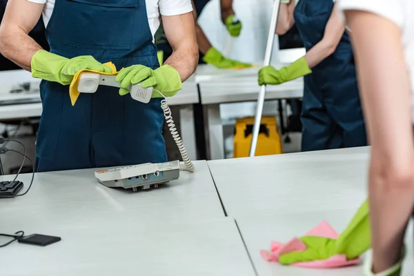 Vue recadrée du nettoyant essuyant téléphone de bureau près du bureau de lavage collègue — Photo de stock