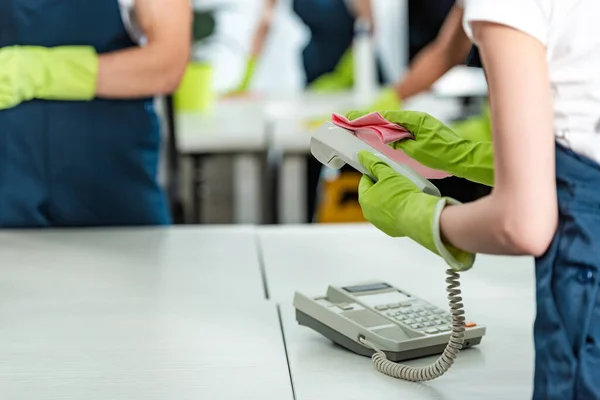 Vista ritagliata di detergente in guanti di gomma pulire il telefono in ufficio — Foto stock