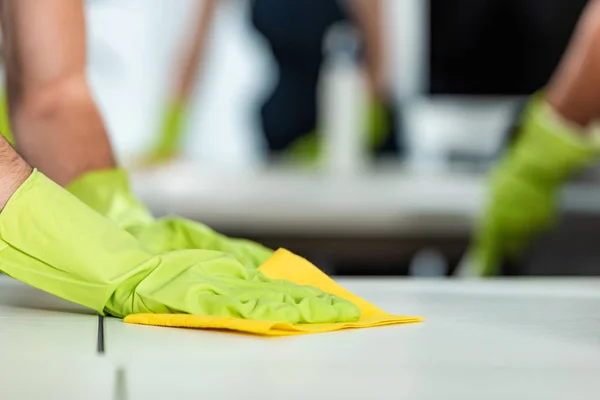 Cropped view of man in rubber gloves cleaning desk surface with rag — Stock Photo
