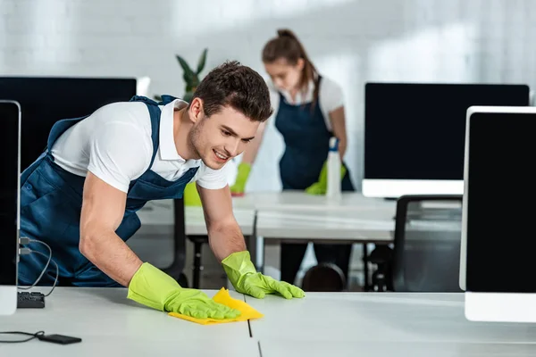 Dos limpiadores jóvenes limpiando escritorios con trapos en la oficina - foto de stock