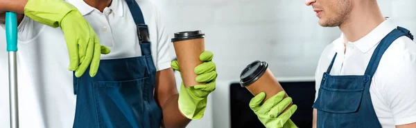 Partial view of multicultural cleaners holding coffee to go in office, panoramic shot — Stock Photo