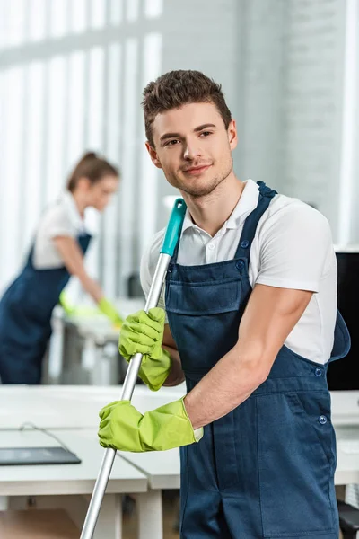 Pulitore sognante guardando lontano mentre collega scrivania ufficio di pulizia — Foto stock