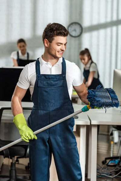 Hübsche Putzfrau lächelt, während sie einen Wischmopp im Büro hält — Stockfoto