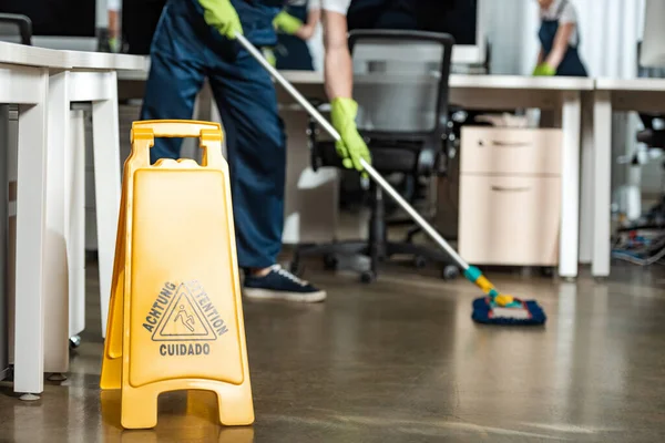 Cropped of cleaner washing floor with mop near wet floor caution sign — Stock Photo