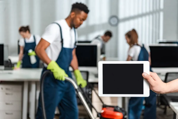 Vista recortada del hombre sosteniendo tableta digital con pantalla en blanco cerca del equipo de limpiadores multiculturales - foto de stock