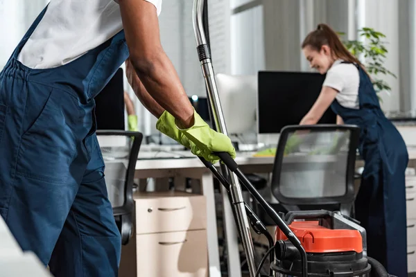 Cropped view of african american cleaner moving vacuum cleaner in office — Stock Photo
