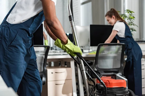 Ausgeschnittene Ansicht von afrikanisch-amerikanischer Reinigungskraft bewegt Staubsauger im Büro — Stockfoto