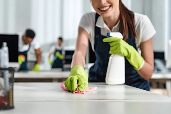 Cropped view of smiling cleaner washing office desk with rag — Stock Photo