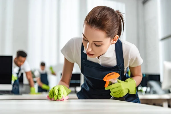 Atento limpiador en uniforme escritorio de oficina de limpieza con trapo - foto de stock