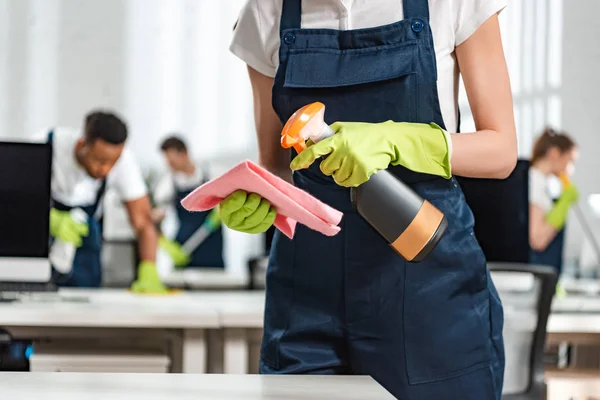 Cropped view of cleaner in uniform spraying detergent on rag — Stock Photo