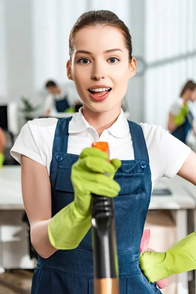 Attractive cleaner holding detergent spray while looking at camera — Stock Photo