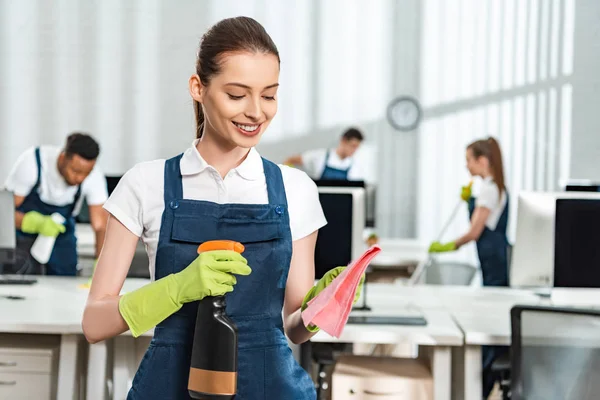 Attractive, smiling cleaner spraying detergent on rag — Stock Photo