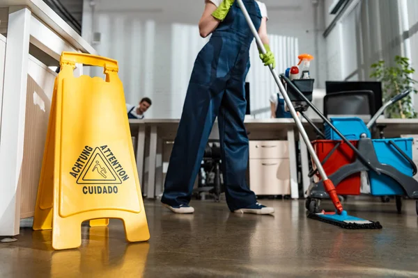 Cropped view of cleaner washing floor with mop near wet floor caution sign — Stock Photo