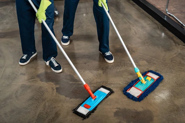 Vista recortada de dos limpiadores lavando piso con trapeadores - foto de stock
