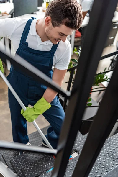 Selective focus of smiling young cleaner washing stairs with mop — Stock Photo