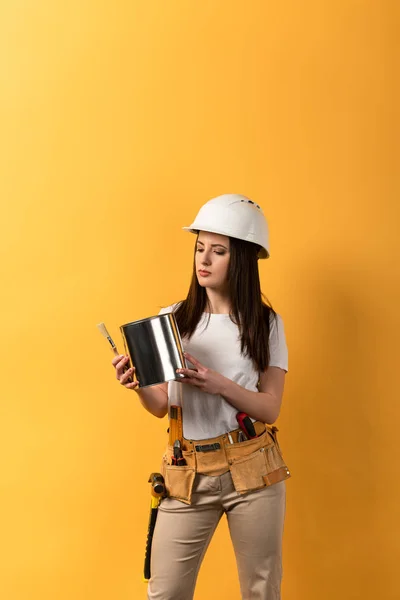 Seriöse Heimwerkerin mit Farbdose und Pinsel auf gelbem Hintergrund — Stockfoto