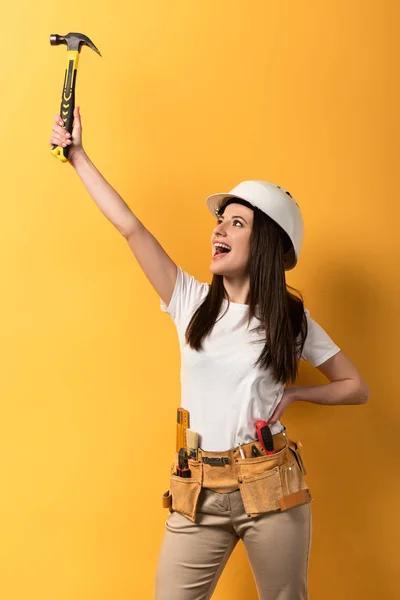 Happy handywoman holding hammer and screaming on yellow background — Stock Photo