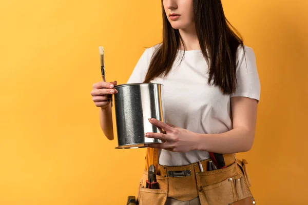 Vista cortada de handywoman segurando lata de tinta e pincel no fundo amarelo — Fotografia de Stock