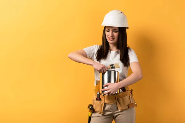 Decepcionado handywoman pintura de apertura puede sobre fondo amarillo - foto de stock