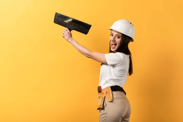 Lächelnde Handarbeiterin im Helm mit Kelle auf gelbem Hintergrund — Stockfoto