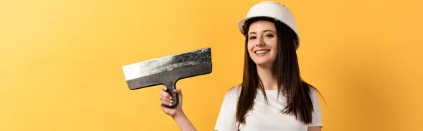 Panoramic shot of smiling handywoman holding trowel on yellow background — Stock Photo