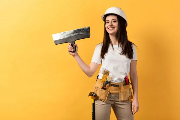 Souriant bricoleur dans casque tenant truelle sur fond jaune — Photo de stock