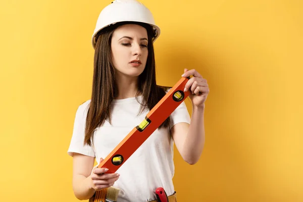 Concentrated handywoman holding spirit level on yellow background — Stock Photo