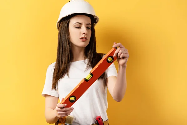 Concentrado handywoman segurando nível de espírito no fundo amarelo — Fotografia de Stock