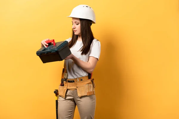Atractivo handywoman en casco celebración caja de herramientas sobre fondo amarillo — Stock Photo